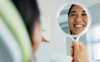 Woman smiling at reflection in handheld mirror