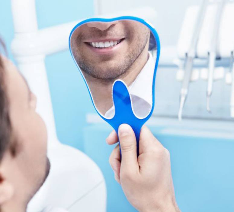 Dental patient’s smile reflected in hand mirror