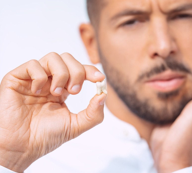 Man holding jaw in pain with one hand and extracted tooth with the other