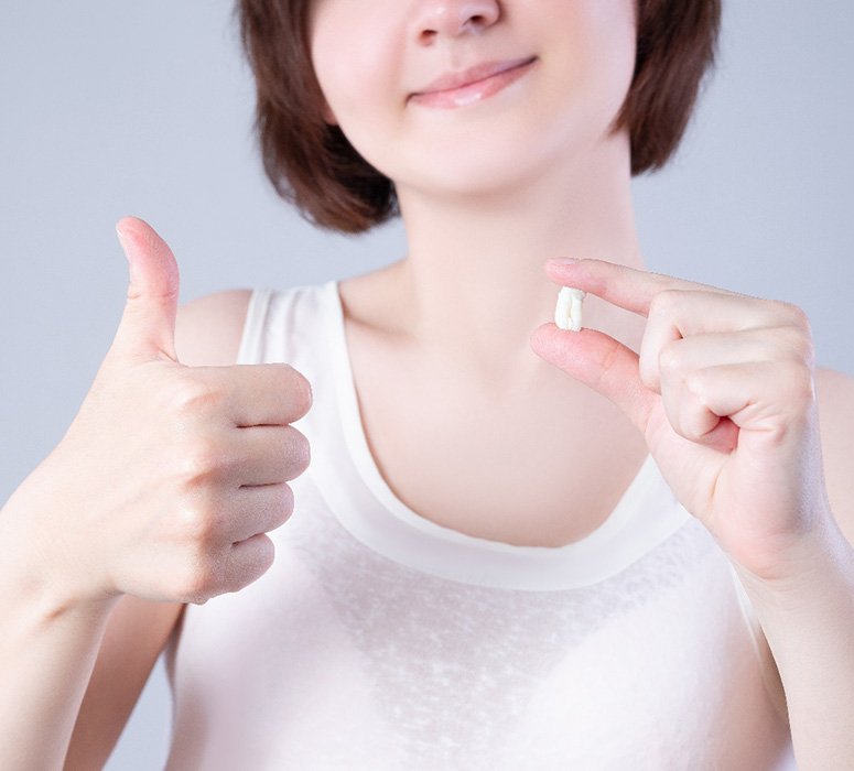 Nose-to-chest view of woman holding extracted tooth and giving thumbs up