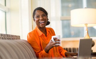 Woman in orange shirt smiling while drinking coffee on couch