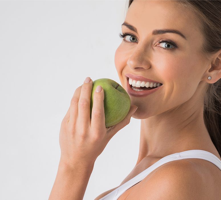 Woman with dental implant replacement teeth eating a green apple