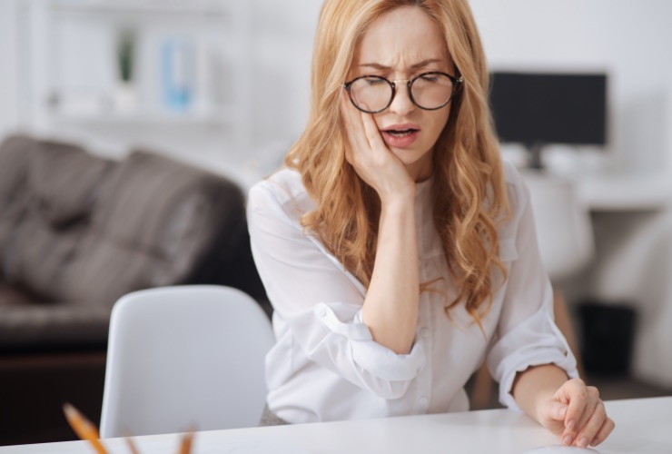 Woman with glasses holding her cheek in pain