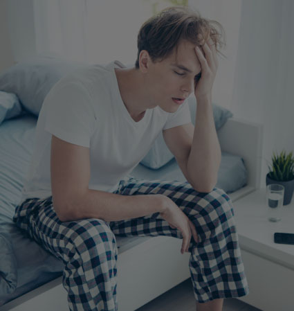 Exhausted man sitting on bed and resting his head in his hand