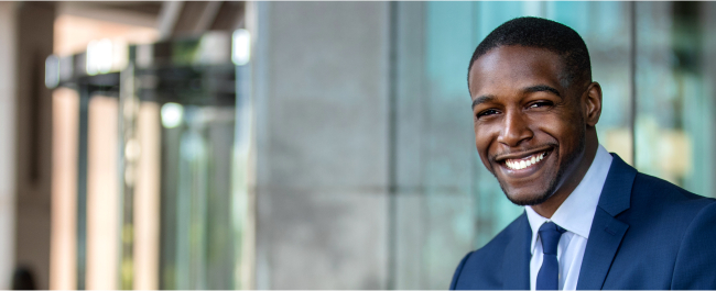 Man in navy blue suit smiling in front of city building