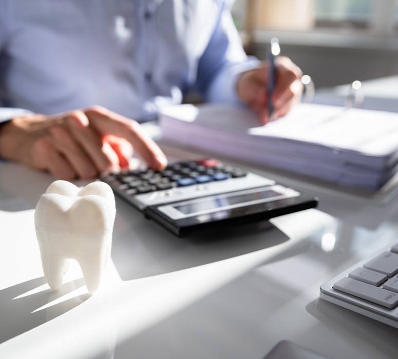 Man using calculator next to model tooth