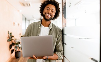 Man smiling while holding laptop in office