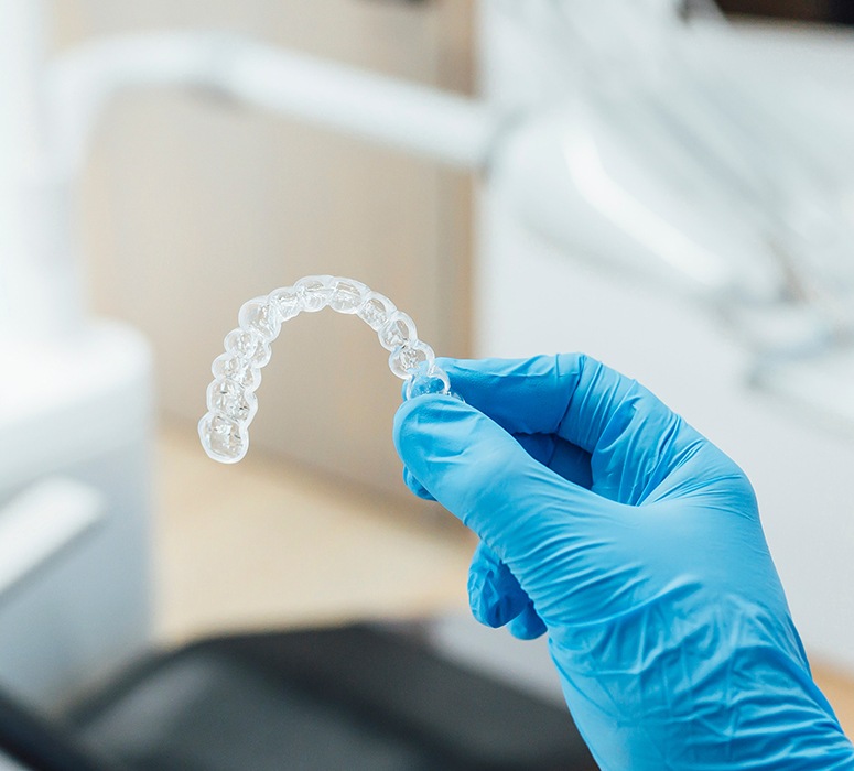 Dentist holding clear aligner with blue gloves