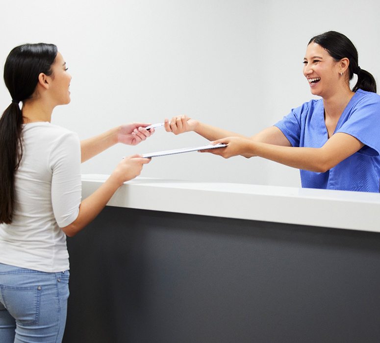 Smiling dental assistant handing patient form