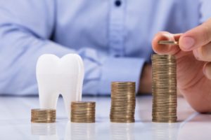 Beachwood dentist with tooth model and increasing piles of coins