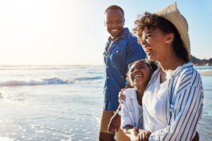 a family smiling and walking on the beach in the sun during the summer