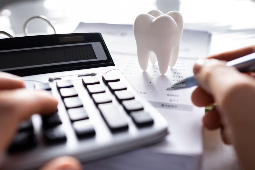 Hands with pen and calculator at desk with large model tooth