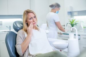 Patient holding jaw and looking miserable in dentist’s chair.